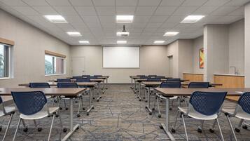 A conference room with a projector screen, tables, chairs, and a carpeted floor.