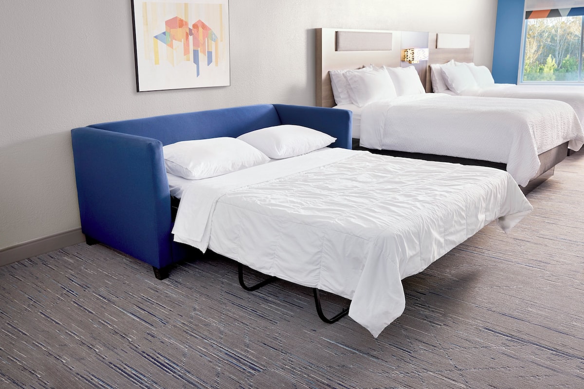 A hotel room with two beds, a blue sofa, a framed abstract painting, and a window with a view.