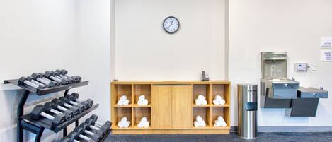 A gym with exercise equipment, a clock, and a water station.