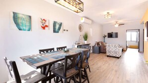 Un coin repas avec une table et des chaises en bois, une cuisine à l’arrière-plan et un espace de vie avec un canapé et un téléviseur.