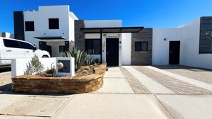 Un bâtiment moderne doté d’un toit plat, d’une entrée sécurisée par un portail et d’un espace paysager agrémenté de cactus.