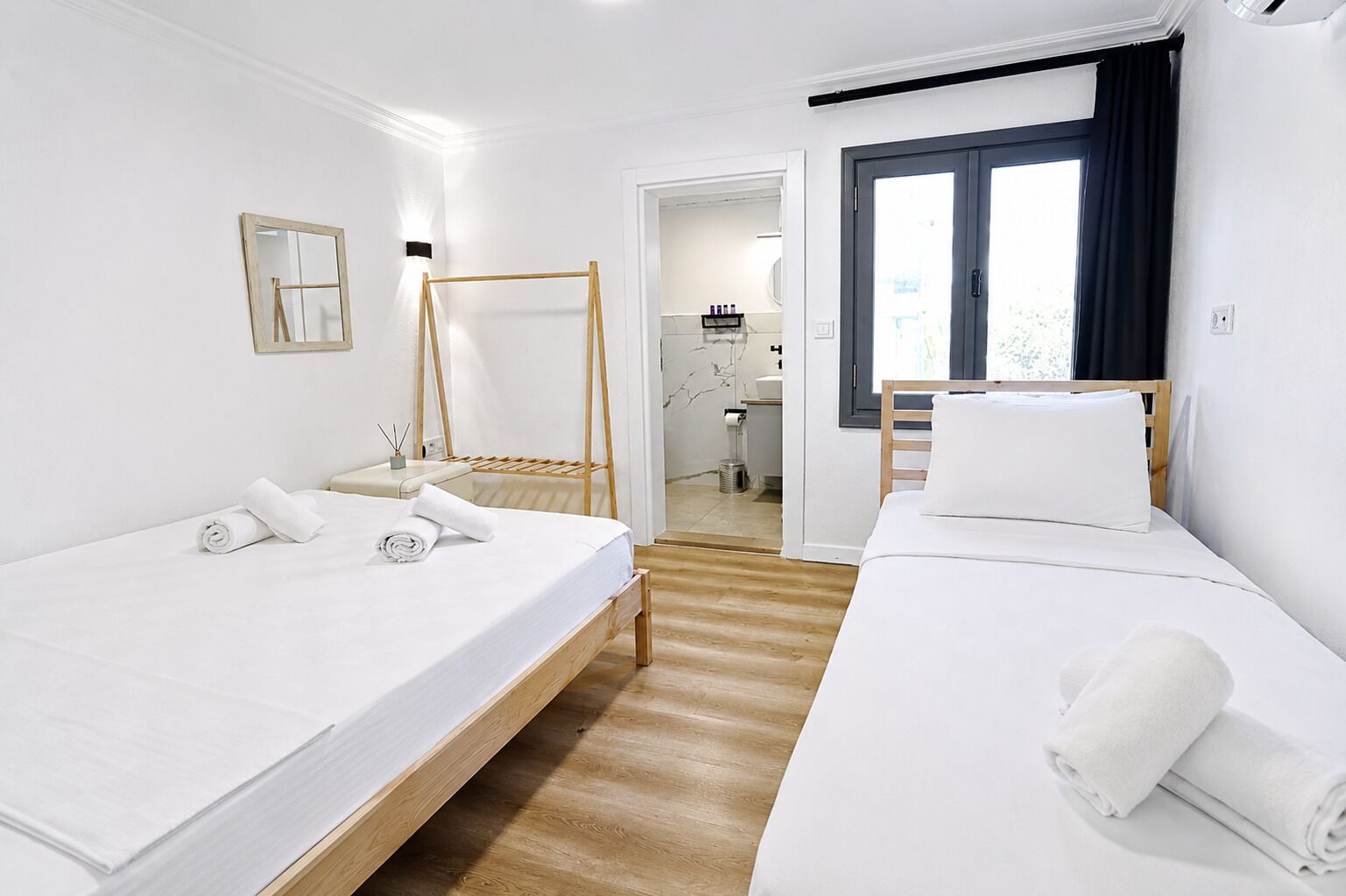 Une chambre d’hôtel avec deux lits, un plancher en bois, un miroir et une vue sur l’extérieur.