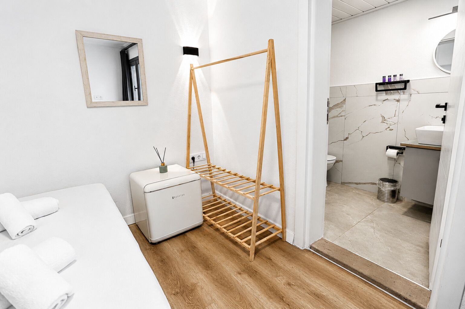 A modern bathroom with a wooden drying rack, a small white appliance, and a mirror on the wall.