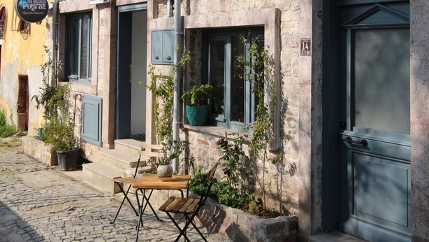 A building with a signboard, a door, windows, and a small outdoor seating area. - The Macaron Poyraz Guesthouse (Ayvalik)