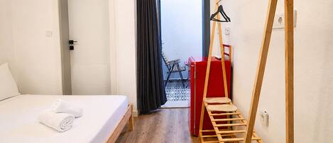 A hotel room with a bed, a wooden ladder, a red suitcase, and a view of the outside.