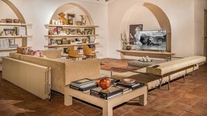 A cozy living room with a sofa, armchairs, a coffee table with books, a TV, and decorative items on shelves. - Linera 10, Emma Villas (Linera)