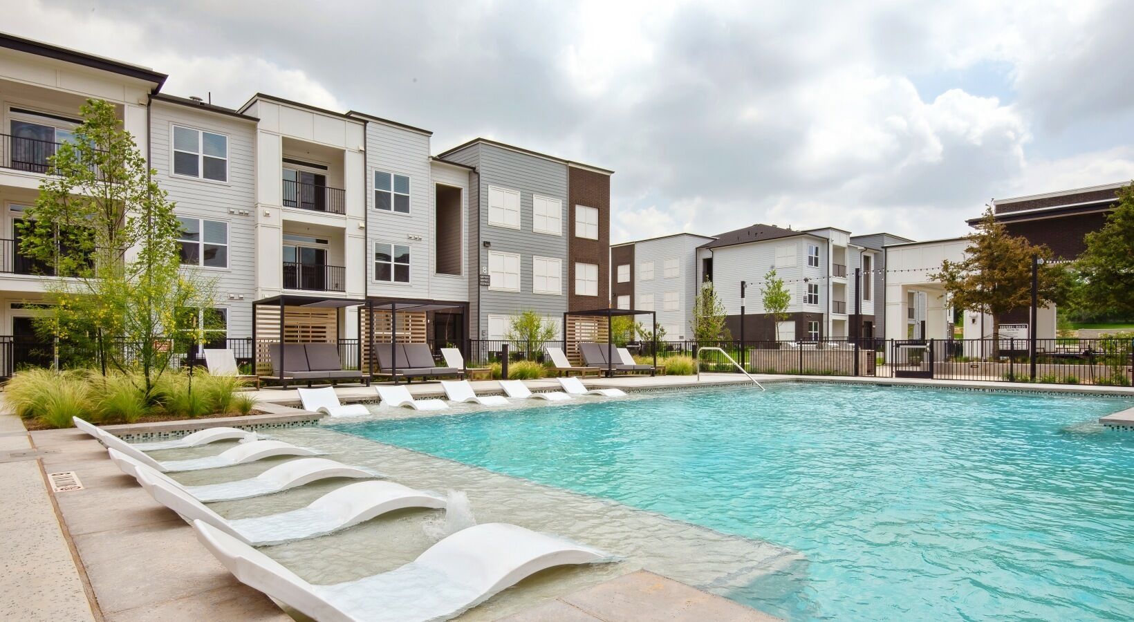 A swimming pool with lounge chairs and a modern apartment building in the background.