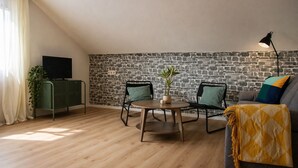 A cozy living room with a stone wall, a sofa, a coffee table, two chairs, a TV on a cabinet, and a lamp. - Holzapfel - Holiday apartment in the Black Forest - 2 bedrooms (Villingen-Schwenningen)