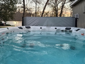 Un bain à remous muni d’une étiquette d’avertissement, entouré d’arbres et d’un bâtiment.