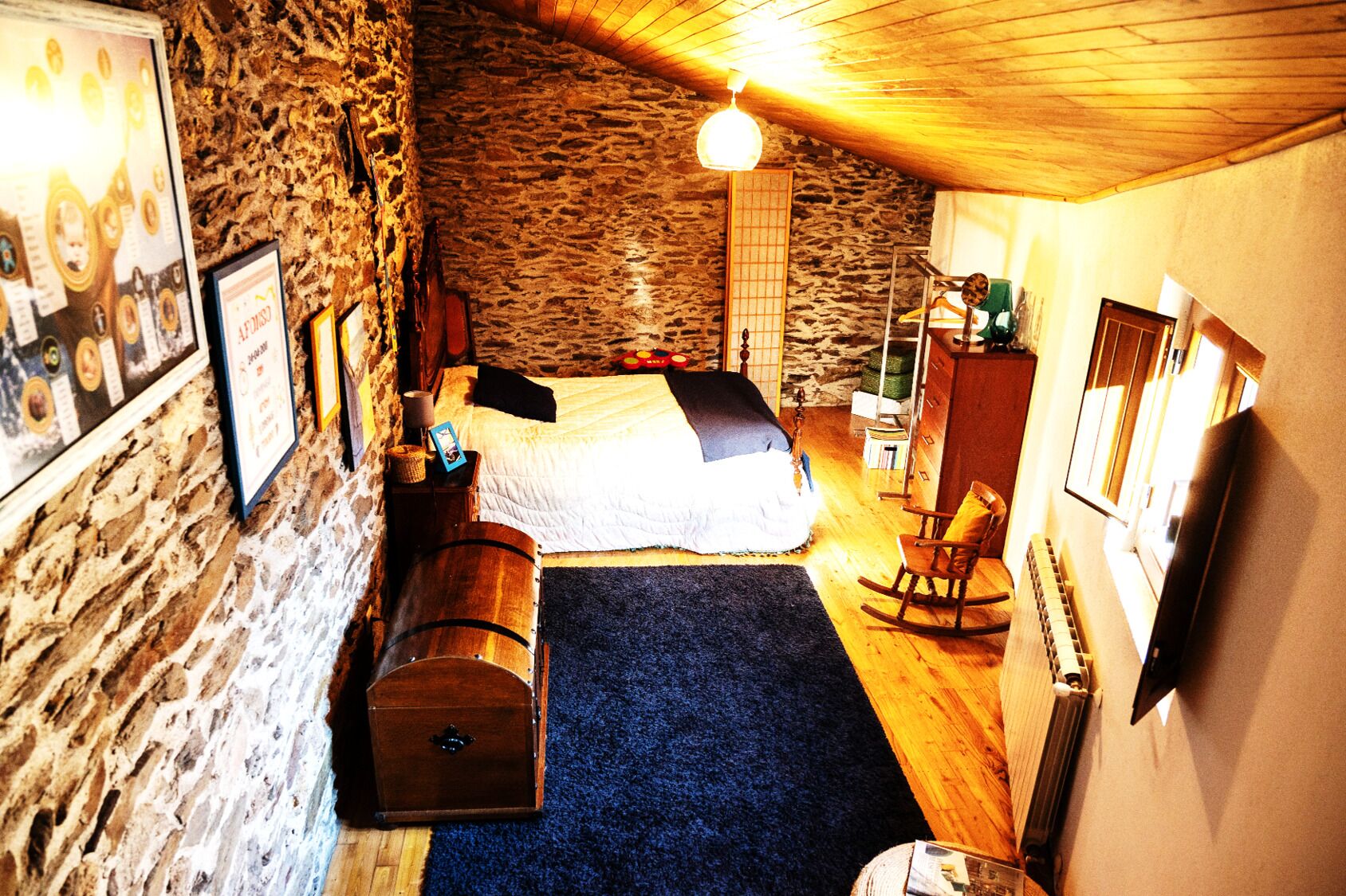 Una habitación acogedora con pared de piedra, una cama, una mecedora y suelo de madera.