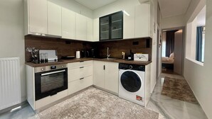 Een moderne keuken met witte kasten, een inbouwoven, een wasmachine en een aanrecht met diverse apparaten.
