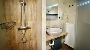 Een moderne badkamer met een douchecabine van hout, een witte wastafel en een spiegel erboven.