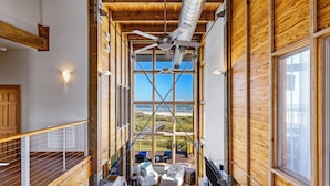 A high-ceilinged interior with wooden beams, large windows, and a view of the outdoors. - Villa Seamone (Galveston)