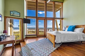 A bedroom with a bed, a desk, a chair, a TV, and a view of the ocean. - Villa Seamone (Galveston)
