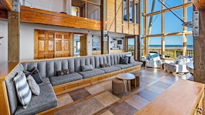 A spacious living area with a large sofa, a round table, and a view of the sea. - Villa Seamone (Galveston)