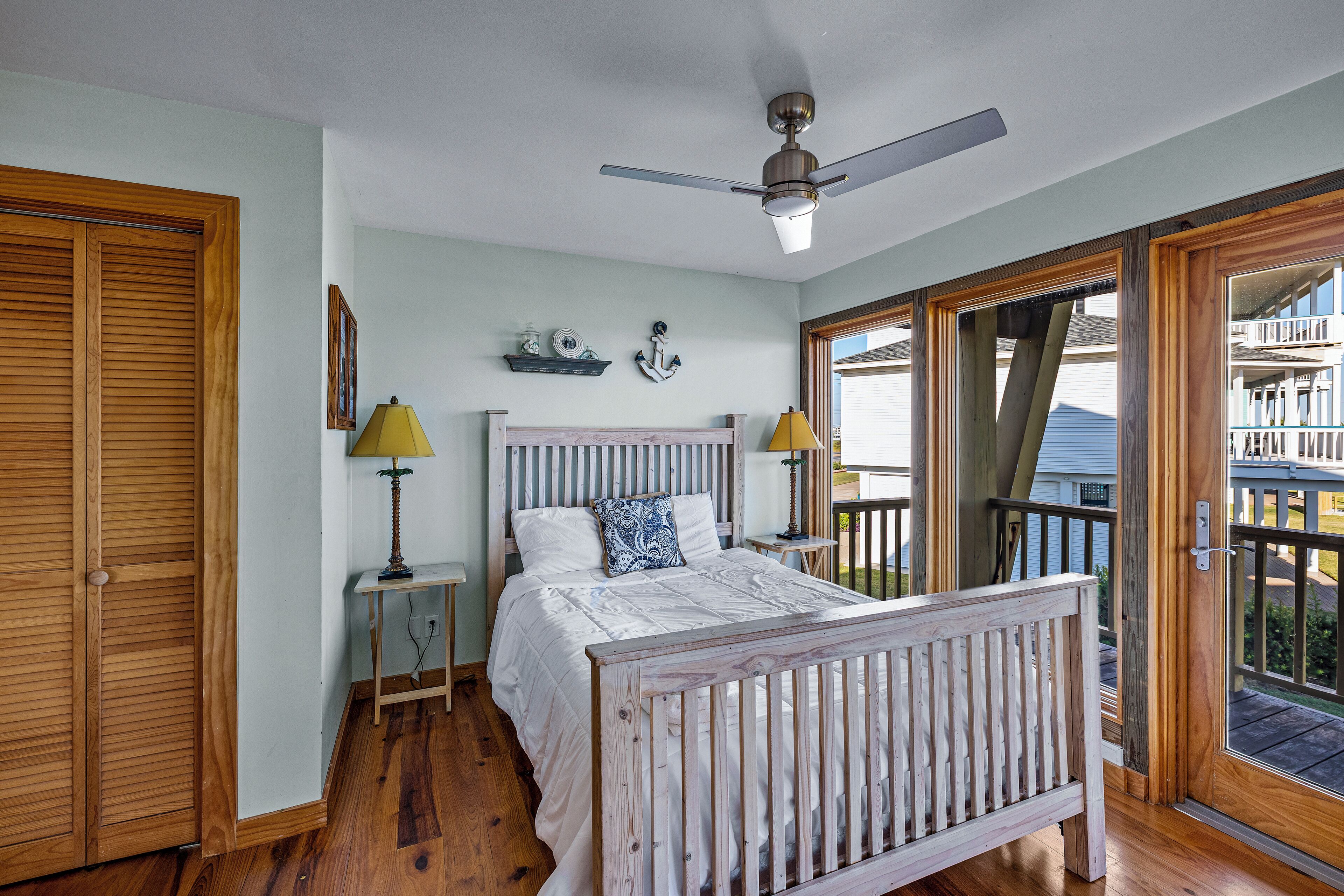 Ein Schlafzimmer mit einem Bett, Holzboden, Deckenventilator und Blick auf einen Balkon.