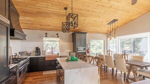 A modern kitchen with a large island, dark cabinetry, and a wooden ceiling.