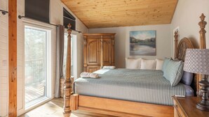 A bedroom with a wooden ceiling, a large bed with a striped bedspread, a wooden wardrobe, and a painting on the wall.