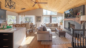 A spacious living area with a wooden ceiling, a fireplace, and a large window providing a view of the outdoors.
