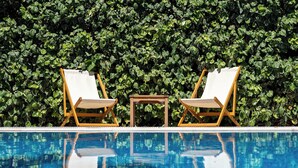 A pool with two lounge chairs and a small table, surrounded by a hedge. - Hotel Dubrava (Budva)