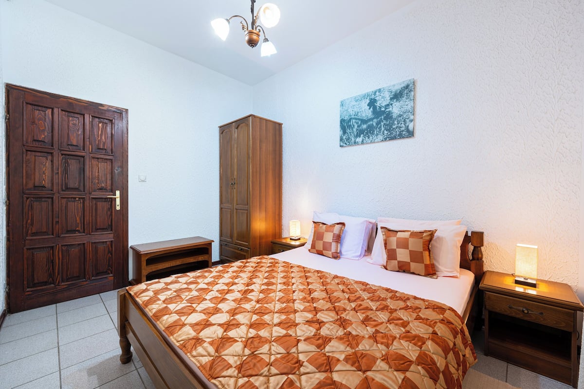 A bedroom with a bed, wooden wardrobe, nightstands, and a ceiling light fixture.