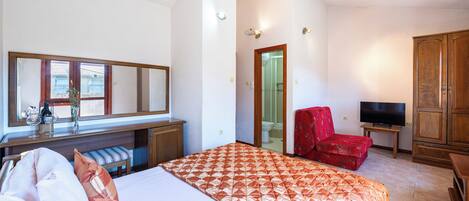 Una habitación de hotel con una cama, un escritorio con espejo, un televisor, una silla roja y un armario.