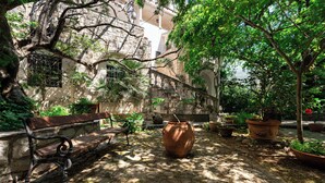 A courtyard with a stone bench, potted plants, and a large terracotta pot. - Hotel Dubrava (Budva)