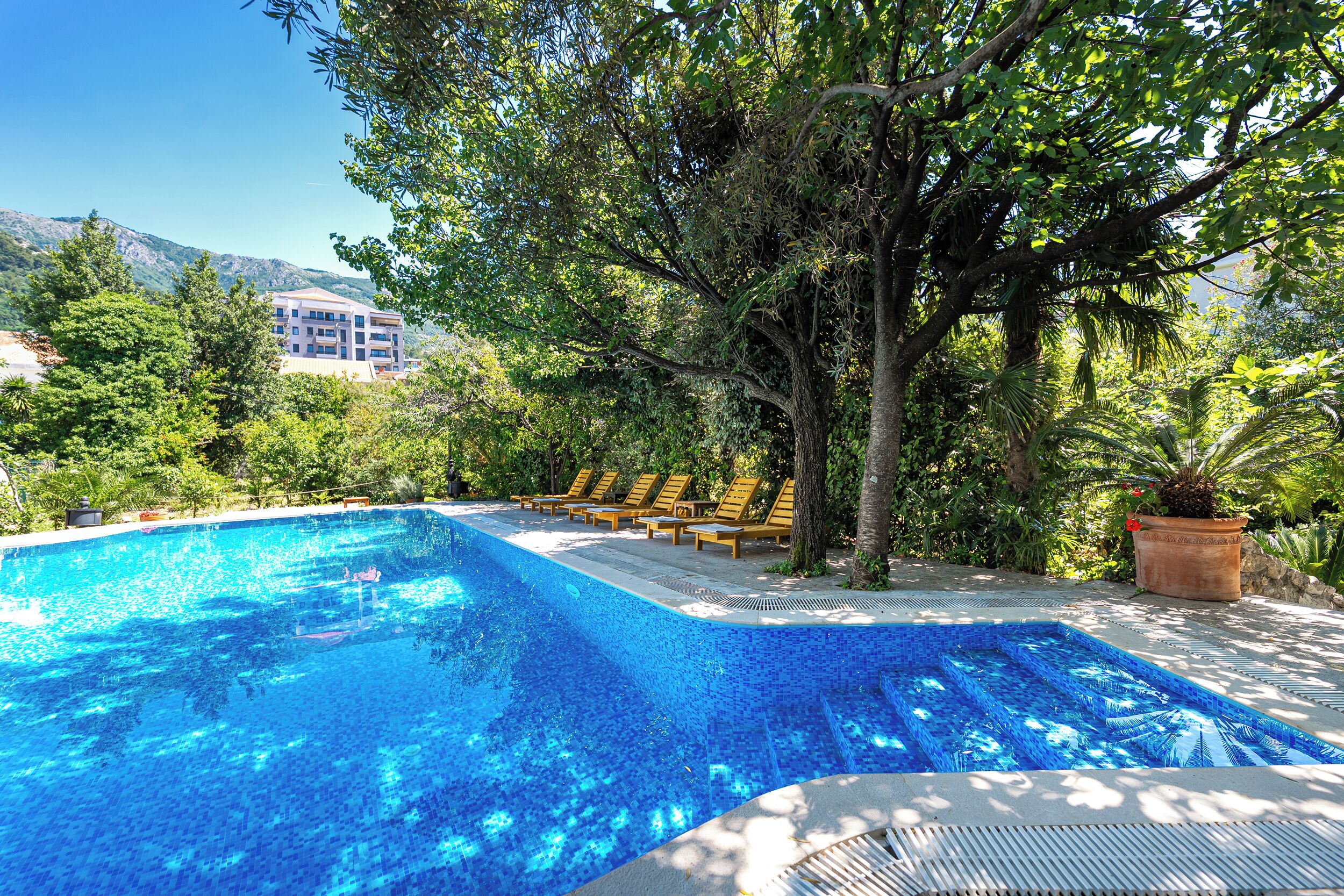 A swimming pool with lounge chairs, surrounded by trees and a mountain in the background.
