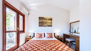A bedroom with a bed, a bedside table with a lamp, a window with an air conditioner, and a painting on the wall. - Hotel Dubrava (Budva)