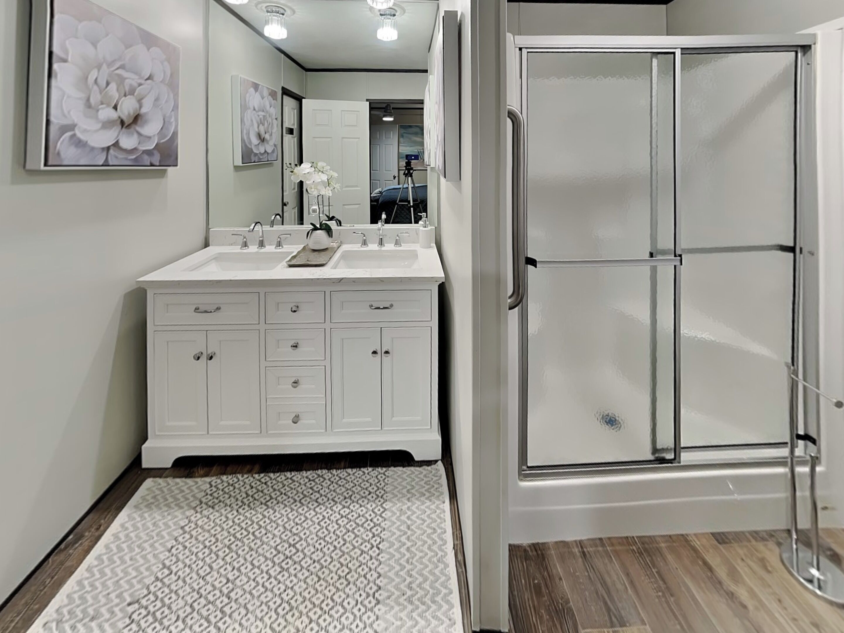 A modern bathroom with a double sink vanity, a glass shower enclosure, and a patterned rug.