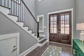 A staircase with a dark wooden handrail and white steps, leading to a wooden door with glass panels.