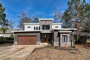Une maison moderne à deux étages, dotée d’une façade en pierre, d’une porte de garage marron et d’un jardin bien entretenu.