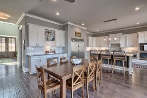 Une cuisine spacieuse avec des meubles blancs, une table à manger en bois et un îlot central intégré avec des sièges.