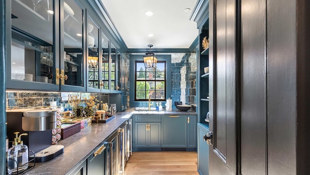 A modern kitchen with dark blue cabinets, a stainless steel range hood, and a large window providing natural light. - The Royce on Pelham - Luxury Family Estate (Newport)
