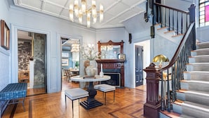 A grand foyer with a wooden floor, a staircase with a dark balustrade, and a chandelier. - The Royce on Pelham - Luxury Family Estate (Newport)