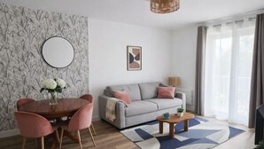 A modern living room with a grey sofa, a round coffee table, and a dining area with a wooden table and pink chairs. - Douce parenthèse - T2 Cosy & warm Montélimar station center within walking distance (Montélimar)