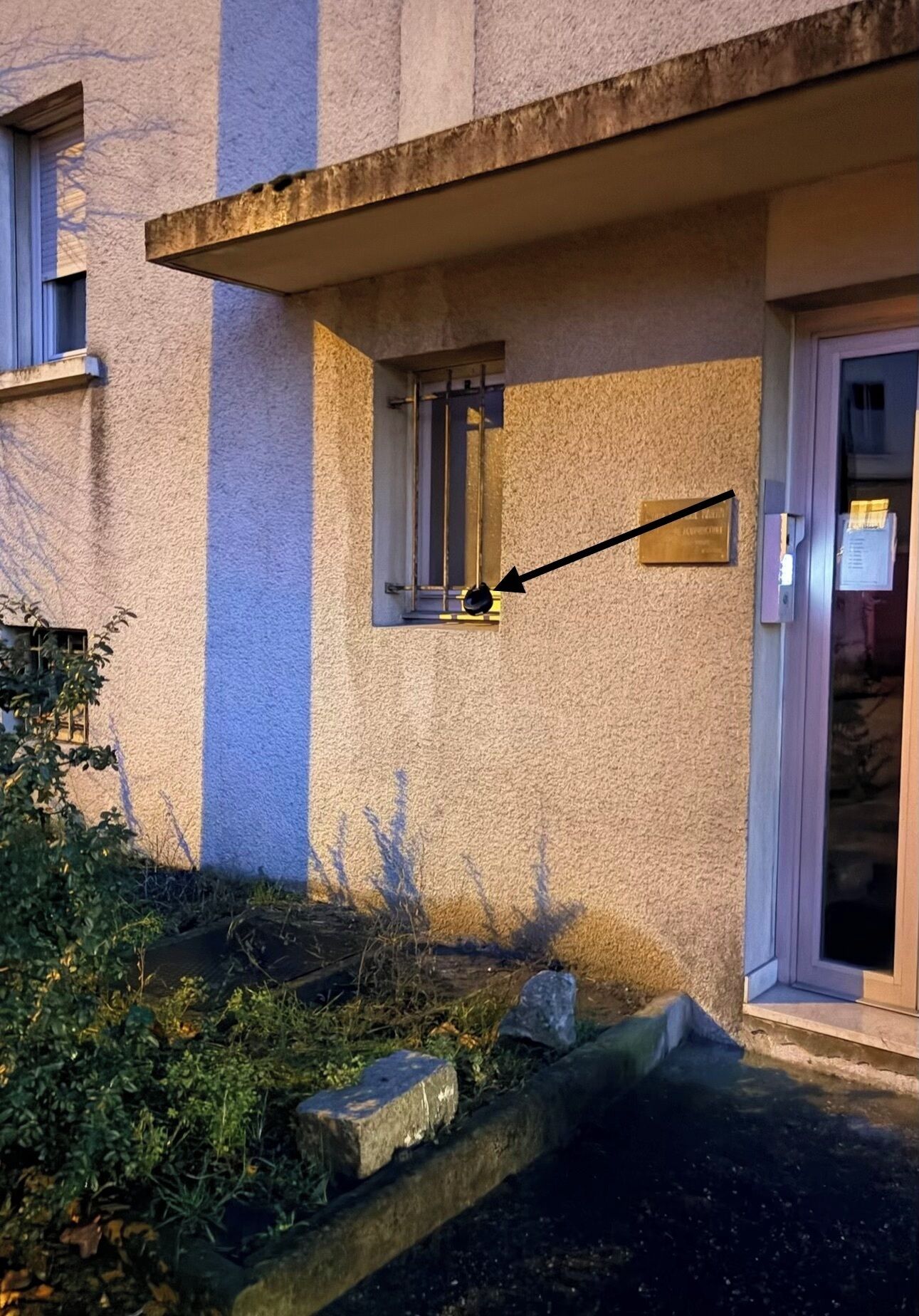 Fachada de edificio con pared texturizada, pequeña ventana con marco metálico y puerta con panel de vidrio.