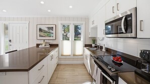 Une cuisine moderne avec des meubles blancs, un four à micro-ondes en acier inoxydable et un plan de travail en bois.