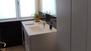 Una cucina moderna con lavello integrato, una finestra con persiane, una pianta in vaso e una plafoniera.