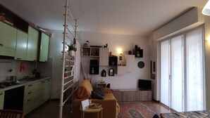 Un ambiente compatto con angolo cottura, divano, televisione e zona pranzo.