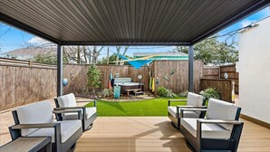 Una veranda coperta con due poltrone bianche imbottite e un tavolo, un piccolo giardino con idromassaggio e un recinto in legno sullo sfondo.
