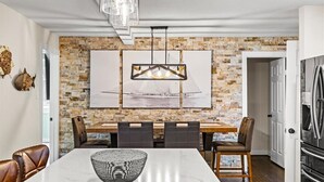Zona pranzo con parete in mattoni, un'ampia pittura, un lampadario moderno e una cucina con elettrodomestici in acciaio inossidabile.