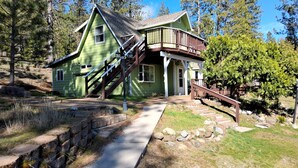 A green house with a wooden staircase leading to a porch.