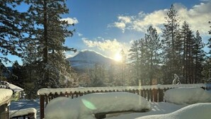 A snowy landscape with a mountain in the background, a wooden fence, and snow-covered trees.
