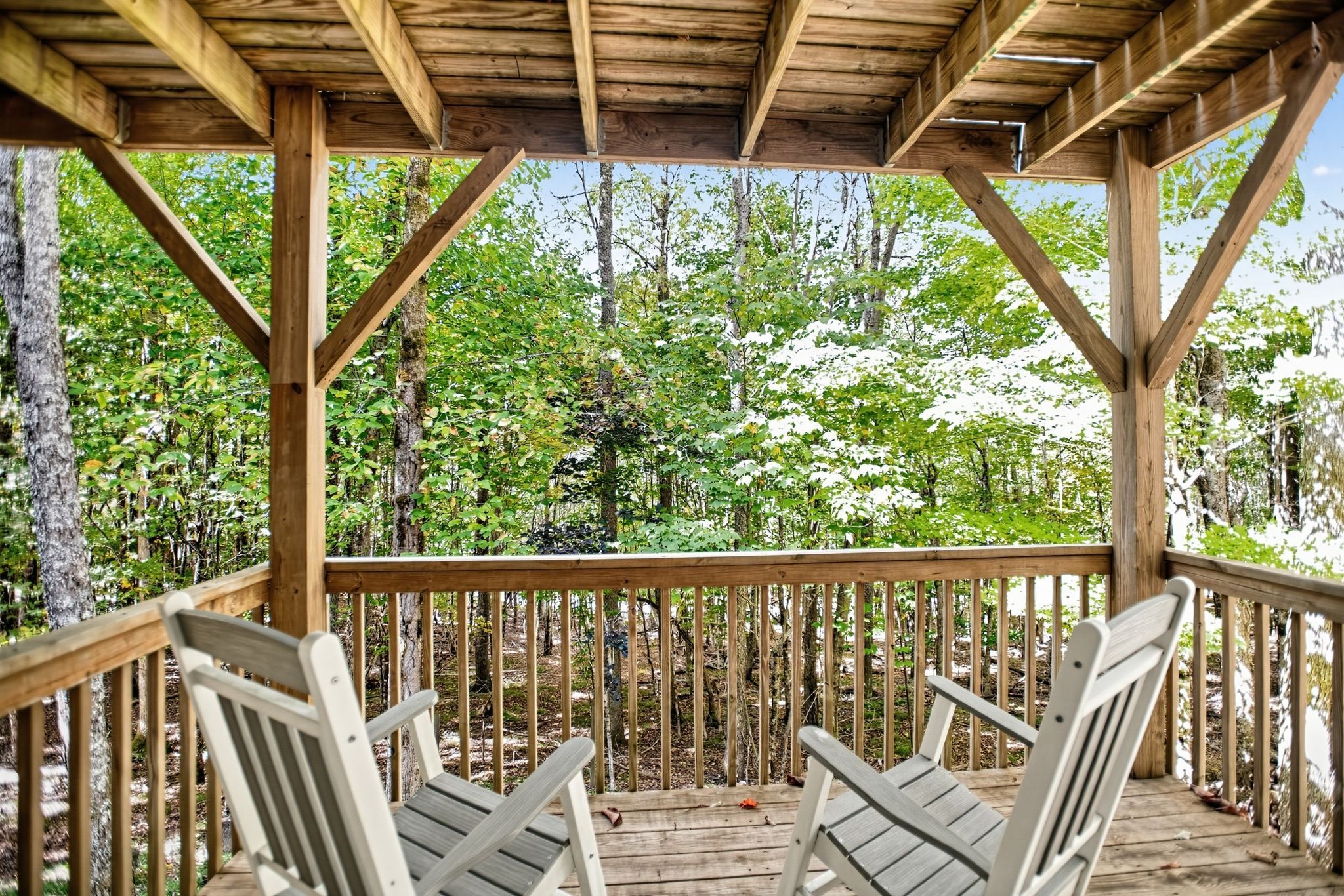 A wooden deck with two chairs and a wooden railing overlooking a forested area.