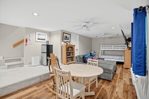 Ein modernes Wohnzimmer mit Esstisch, Stühlen, einer Couch, einem Bücherregal und einem Etagenbett.