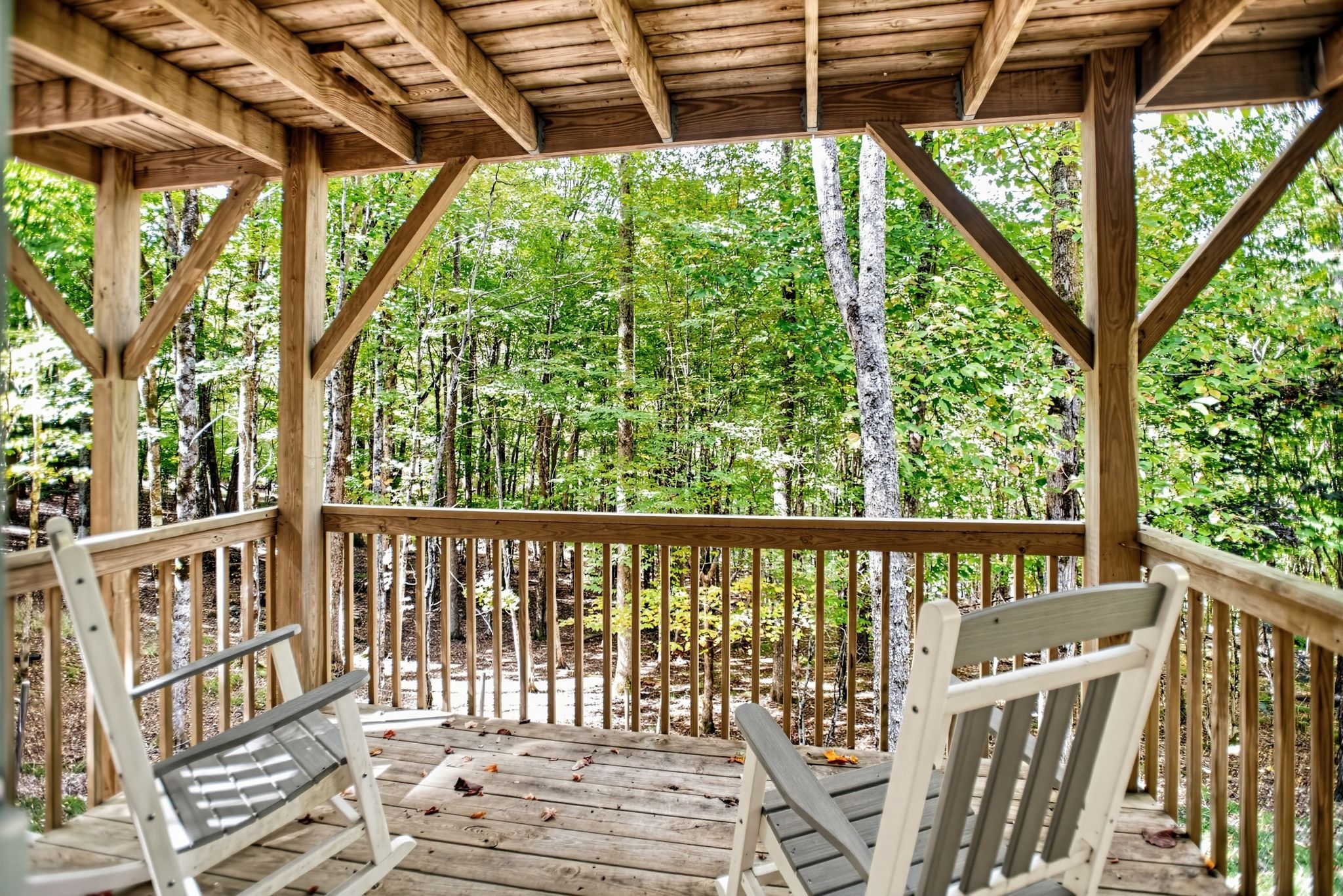 Ein hölzerner Pavillon mit Holzboden und Geländern, umgeben von Bäumen.