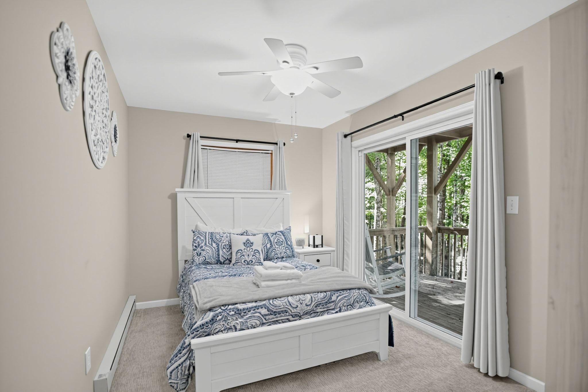 A bedroom with a bed, a ceiling fan, a window with curtains, and a view of the outdoors.