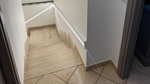 Una escalera estrecha con barandilla, paredes blancas y una puerta con sensor a la derecha.