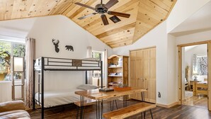 Une pièce avec un lit superposé, un plafond en bois, une table avec des bancs et un ventilateur de plafond.